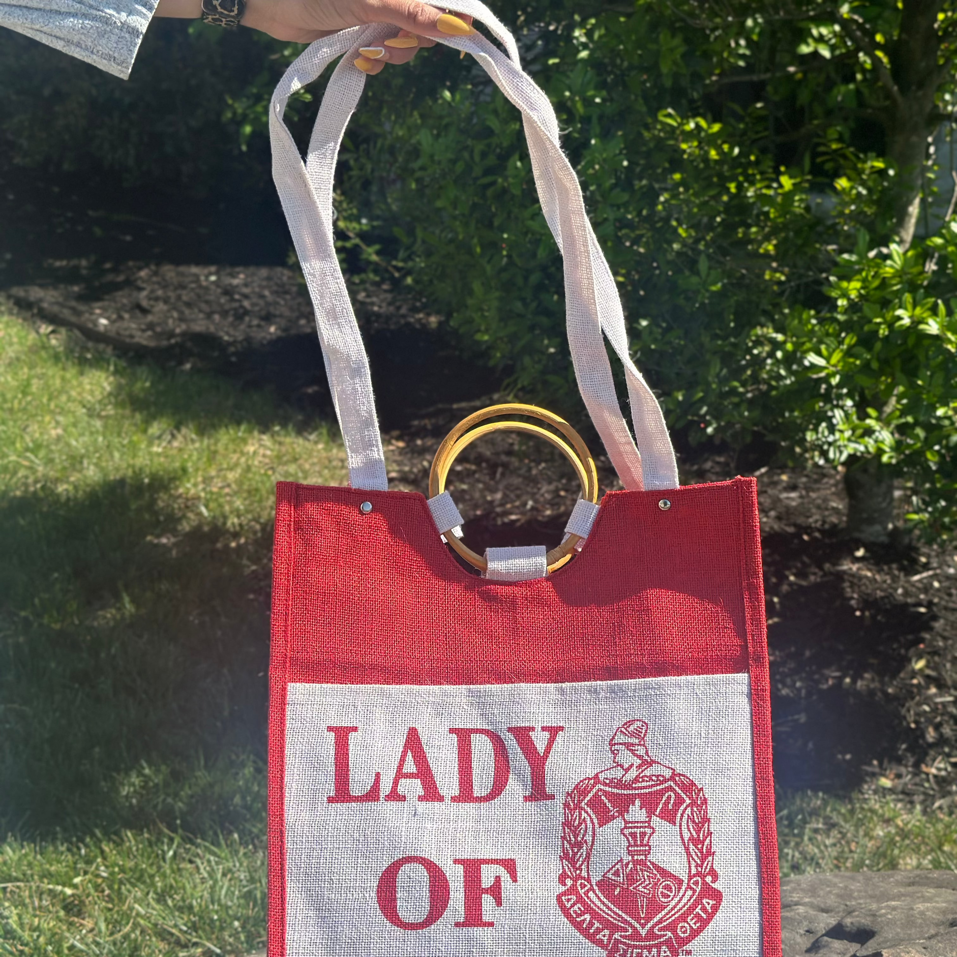 Red and white tote bag with 'Lady of Delta' text and logo on a stone surface.
