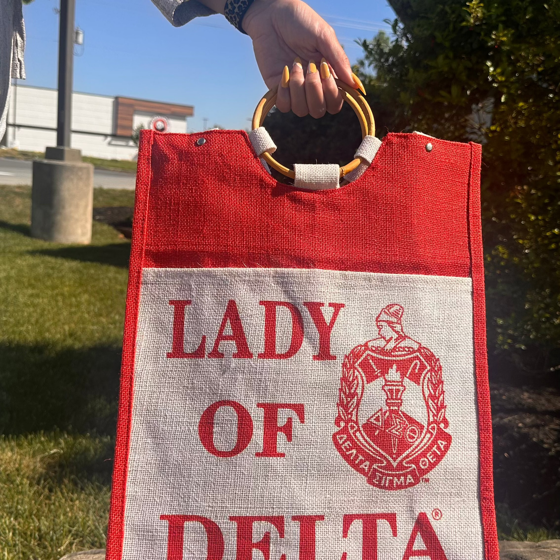 Red and white bag with 'Lady of Delta' text and logo held by a person outdoors.